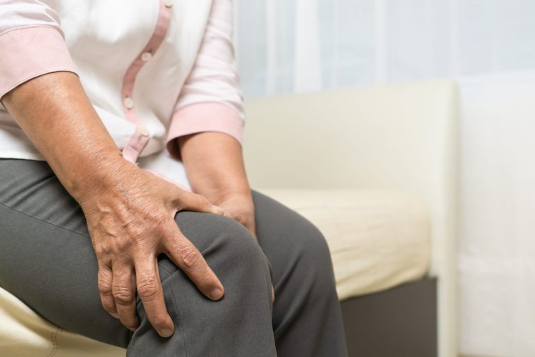 why knee pain increases with age showing elderly person holding knee while sitting with joint discomfort